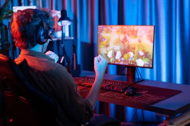 Genç oyun flamasının sunucu kanalı Moba ile savaş meydanında çoklu oyun takımıyla dövüşmeyi kazanıyor, bilgisayar monitöründe kulaklık takıyor ve neon dijital ışık modern odasında arka plan görüntüsü takıyor. Toplayıcı.