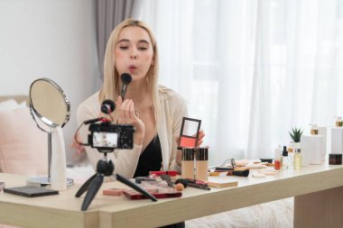 Sosyal medya için güzellik ve kozmetik video içeriği hazırlayan genç bir kadın. Güzellik blogcusu, seyircilere ve takipçilere rimel sürmeyi öğretirken kameraya gülümsüyor. Blithe