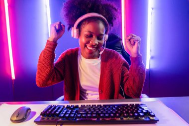 Oyun flama, Afrikalı kız Esport yetenekli takımıyla online kavga ediyor. Neon renkli aydınlatma odasında kulaklık takıyor. Rakiplerini kazanmak için strateji planlayan diğer oyuncularla konuşmak. Tatlandırıcı.