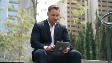 Green City 'de otururken tablet üzerinde çalışan iş adamlarına yakın durun. Düşük açılı kamera, yönetici tabletini kullanarak uzaktan çalışırken finansal veri analizini tarıyor. Urbane.