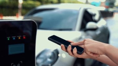 Modern iş kadını akıllı telefonun 3D hologramından batarya durumunu kontrol ederken EV arabasının şarj olan enerjisini kontrol eder. Gelecekteki EV otomotiv teknolojisinin yenilikçi teknolojik gelişimi. İnceleyin