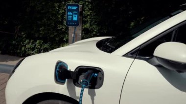 Doğal yeşil araba parkındaki ekolojik temiz enerji şarj istasyonundan gelen fütürist akıllı EV şarj aletinin şarj ettiği elektrikli araba. Alternatif enerji kullanan gelecekçi çevre dostu elektrikli araba. İnceleyin