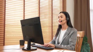 Kadın çağrı merkezi operatörü ya da müşteri hizmetleri çalışanı, müşteriye yardım etmek için kulaklıkla konuşurken çalışma alanı üzerinde çalışıyor. Profesyonel modern iş hizmeti. Blithe