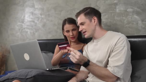 若いカップルは クレジットカードで支払うためにラップトップ上のオンライン決済アプリとデジタルウォレットを使用してホームベッドルームに座っています モバイルインターネットを介して商業ショッピングとモダンな購入 アディット — ストック動画