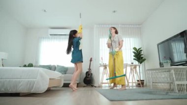 Beyaz anne ve Asyalı çocuk birlikte ev işi yapıyor ve müzik eşliğinde dans ediyorlar. Çekici anne ve kız modern yatak odasını temizlerken şarkı söyleyip rahatlatıcı müziğe atlıyorlar. Yaşam tarzı. Pedagoji.