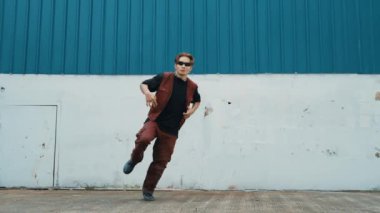 Beyaz arka planda break dans pratiği yapan yakışıklı bir sokak dansçısı. Hip hop tarzı giyinen sporcu, mavi arka planlı bir sokakta müzik eşliğinde ayak sesleri çıkarıyor. Açık hava sporu 2024 hiphop..