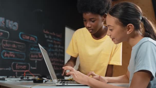 快乐的非洲男孩指着笔记本电脑屏幕 而可爱的女孩则在打字笔记本电脑编码或程序设计系统 在Stem技术课上手握笔记本电脑的教师教学程序 — 图库视频影像