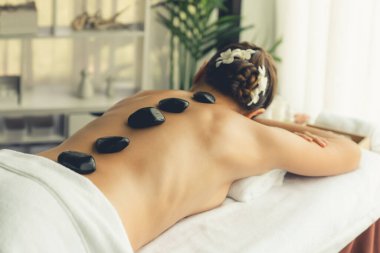 Lüks tatil köyündeki kaplıcalarda sıcak taş masajı. Gün ışığı sükunet ortamında, mutlu kadın müşteri bazalt taş masajından zevk alıyor. Rahatlatıcı bir sıcaklıkla vücudun üzerinde süzülüyor. Sessiz.