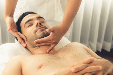 Beyaz adam stres önleyici kafa masajından ve lüks bir tatil beldesi veya otel spa salonundaki modern ışık ortamında yüz güzelliği eğlencelerini şımartmaktan hoşlanıyor. Sessiz.