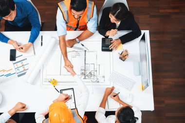 Çeşitli inşaat mühendisi ve müşteri gruplarından oluşan üst düzey panorama, mimari proje üzerinde başarılı bir anlaşma yaptıktan sonra el sıkışma, inşaat planını gözden geçirme ve toplantı masasında plan oluşturma konularında ihtiyatlı.