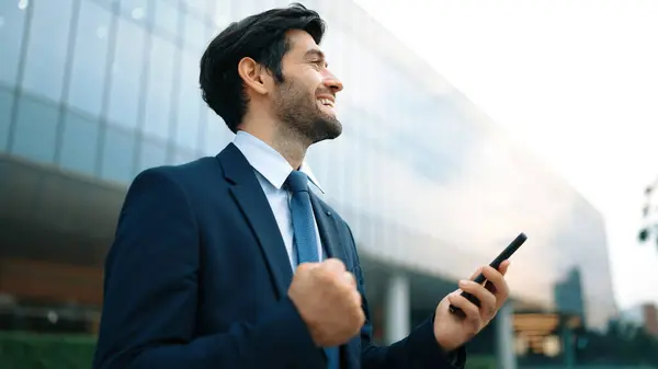 Successful business man celebrate increasing sales while standing. Happy project manager or leader proud with successful project, getting a promotion, getting a job while holding a phone. Exultant.