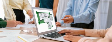 Profesyonel mimar, mimari dökümanlar etrafa saçılmışken toplantı masasındaki planların değiştirilmesiyle ilgili tartışmalarda çevre dostu evin planına karar veriyor. - Yakın çekim. Tanımlama