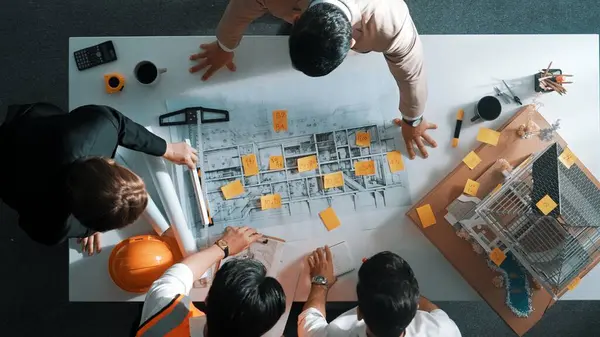 Top down view of skilled engineer team compare between blueprint and house plan. Aerial view of group of architect or designer discussing and point note to brainstorm about blueprint. Alimentation.