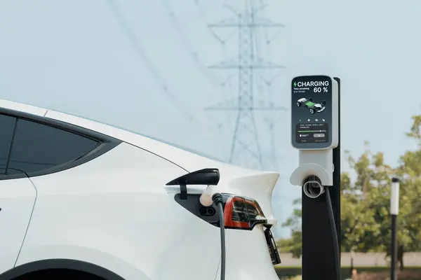 Electric vehicle or EV car recharge battery at charging station connected to power grid tower electrical industrial facility as electrical industry for eco friendly vehicle utilization. Expedient