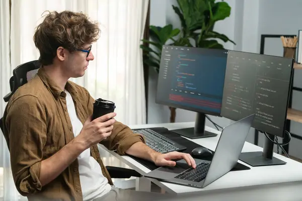 Working IT developer holding coffee cup with looking online software on pc at modern office on coding application screens, creating updated latest program firmware information version concept. Gusher.