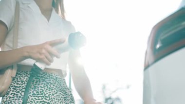Yavaş çekim güneş ışığı arka plan aydınlatması EV elektrikli arabasıyla gezen kadın yazın yeşil sürdürülebilir şehir bahçesinde şarj oluyor. Elektrikli araç iç organlarından yeşil kentsel sürdürülebilirlik yaşam tarzı
