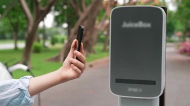 Ulusal Park veya Yaz Ormanı 'ndaki tatil gezisi sırasında EV şarj istasyonundan elektrik aküsü almak için akıllı telefon internet bankacılığı başvurusu yapan bir kadın. Yükselt
