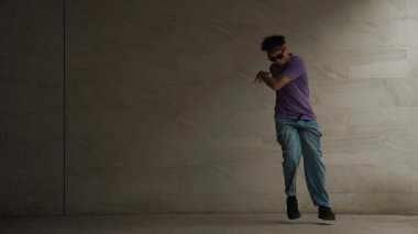 Zeki sokak dansçısı, gri arka planlı bir binada break dansçı hareketi yapıyor. Genç ve çekici koreograf enerjik ve aktif hareket ediyor. Açık hava sporu 2024. Yumuşak bir şekilde..