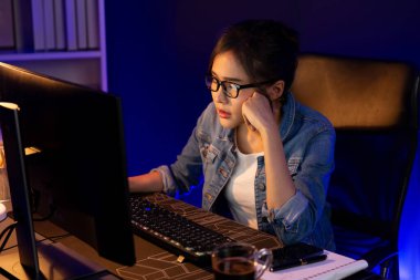 Stresli, genç, güzel Asyalı yaratıcı proje yaratıcısı sosyal medyayı araştırmak için bilgisayara bakıyor ve geceleri daha çok neon modern ofisin planlama kanalı stratejisine ulaşılıyor. Taktik.