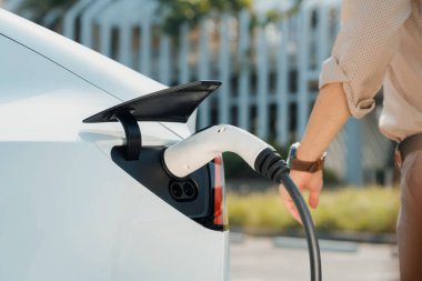Genç adam, şehrin ticari otoparkındaki şarj istasyonundan elektrikli araba aküsünü şarj etmek için EV şarj aleti koymuş. Sürdürülebilir çevre dostu şehir yolculuğu için şarj edilebilir EV araba. Yararlı
