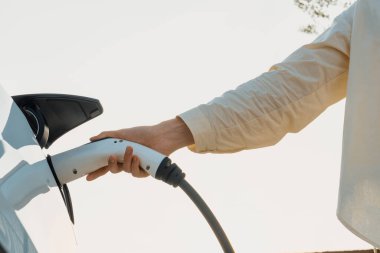 Genç bir kadın şarj aletini şarj istasyonundan elektrikli araba aküsünü şarj etmek için kullanmış. Sürdürülebilir çevre dostu seyahat konsepti için alternatif enerji ve şarj edilebilir EV araba. Yararlı