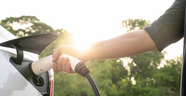 Yolculuk sırasında doğal ormanlarda ya da güneş ışığı alan ulusal parklarda elektrikli araba için şarj olan bir adam. Tatil ve tatil boyunca çevre dostu seyahat. Büyüleyici Panorama