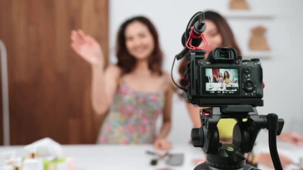 リアビュー一覧カメラ画面表示2人の女性インフルエンサーがライブストリーミングビデオレビューメイクアップソーシャルメディアやブログを撮影します マーケティングレコーディングのための化粧品の鮮やかなスタジオ照明を持つ少女 — ストック動画