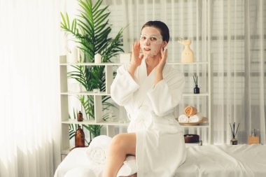 Kaplıca salonunun sakin, modern gün ışığı atmosferi, kadın müşteri poz veriyor ve yüz maskesi ile gençleştiriyor. Yüz bakımı ve güzellik kozmetolojisi prosedürü. Sessiz.