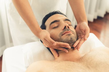 Beyaz adam stres önleyici kafa masajından ve lüks bir tatil beldesi veya otel spa salonundaki modern ışık ortamında yüz güzelliği eğlencelerini şımartmaktan hoşlanıyor. Sessiz.