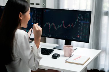 Başarılı genç Asyalı iş kadını, modern ofisteki bilgisayar ekranlarında dinamik iş grafiği üzerine borsada yumruklaşarak en yüksek karı elde ediyor, finansal teknolojiyi analiz ediyor. Taktik.