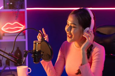 Genç ve güzel Asyalı yayıncının sunucu kanalı, dinleyicilerle sosyal medyada müzik dinliyor, pastel kulaklık takıyor, kapalı alanda neon ışıklı stüdyoda şarkı söylemek için mikrofon kullanıyor. Taktik.