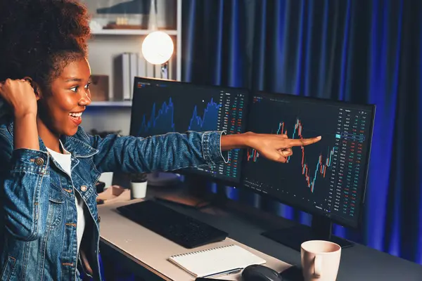 stock image African woman blogger exited with happy face, pointing on screen with valued stock market achievement at high profit. Concept of exchange investment online in trading application on pc. Tastemaker.