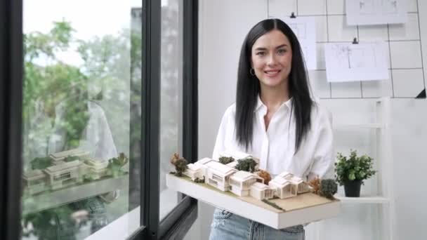 Красивий Молодий Кавказький Архітектор Показує Модель Будинку Стоячи Посміхаючись Упевненістю — стокове відео