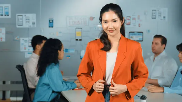 Asian professional businesswoman standing with confident at creative business meeting. Beautiful confident leader posing while diverse business people discussion about using Ux and Ui design