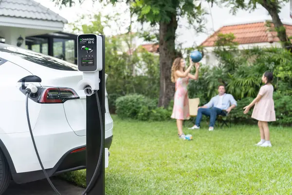 自宅の充電ステーションから電気自動車の充電に焦点を当て 幸せで遊び心のある家族が一緒に遊んでいます よりよい未来のための代替および持続可能なエネルギーを使用するEv車 シンクロノス — ストック写真