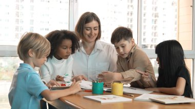 Çizim kitabında işaret kullanarak çeşitli öğrencilerin ve zeki öğretmen çizimleri ve boyamaları mutlu olsun. Çok kültürlü, zeki bir öğrenci yetenekli beyaz bir eğitmenle konuşurken çizim kitabı kullanıyor. Etkinlik.