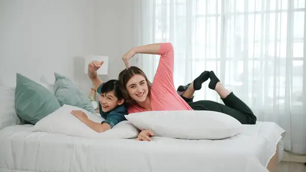 Happy asian daughter and smart mom lie on bed while looking at camera. Energetic family spend time and prepare to sleep together. Cute girl and mom smile to camera show love and affection. Pedagogy.