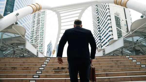 Smart caucasian businessman walking up stairs surrounded by urban view. Back view of ambitious project manager finding challenging job or investment opportunity at city with modern building. Urbane.