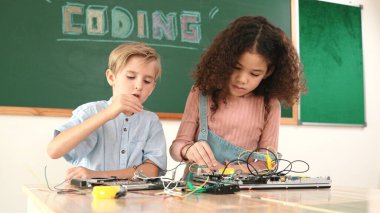 Akıllı kız tornavida kullanarak elektronik tahtayı tamir ederken ayakta duruyor. Mutlu öğrenci ve mutlu beyaz çocuk elektrik sistemini denetlemek için birlikte çalışıyor. Gemide çalışan meraklı çocuklar. Pedagoji.