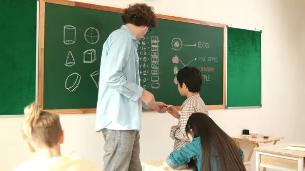 Asian boy finish writing answer while teacher clapping hands to encourage child. Attractive student walking back to his seat while teacher applause and clap hand to schoolboy at Math lesson. Pedagogy.