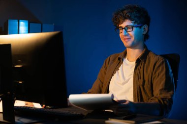 Genç işadamı, Neon Light Modern Ofis 'teki yeni proje surround çalışma masası için kağıt üzerinde tasarım düşünüyor. E-posta ile hediye göndermeden önce not defterine yeni bir iş düşünüyorum. Toplayıcı.