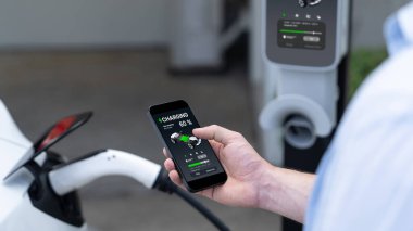 Modern çevre dostu adam EV şarj istasyonundan elektrikli aracı şarj ediyor. Akıllı telefondan şarj gösterimini optimize etmek için enerji kullanımını takip etmek için yenilikçi EV teknolojisi kullanımı. Senkronlar