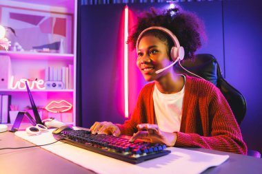 Neon renkli aydınlatma odasında kulaklık takan Afrika kökenli Amerikalı kız flamalı Esport yetenekli takımıyla online dövüş yapıyor. Rakiplerini kazanmak için strateji planlayan diğer oyuncularla konuşmak. Tatlandırıcı.