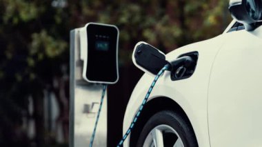 Doğal yeşil araba parkındaki ekolojik temiz enerji şarj istasyonundan gelen fütürist akıllı EV şarj aletinin şarj ettiği elektrikli araba. Alternatif enerji kullanan gelecekçi çevre dostu elektrikli araba. İnceleyin