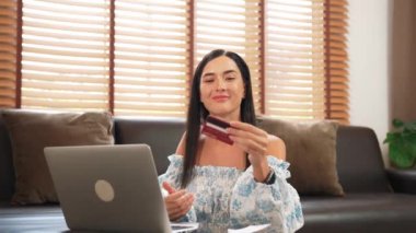 Genç bir kadın internet bankacılığı için kredi kartıyla dizüstü bilgisayar kullanıyor. Evinde online ödeme kapısı ile E ticareti yapıyor. Banka kartıyla modern ve kullanışlı online satın alma. Blithe