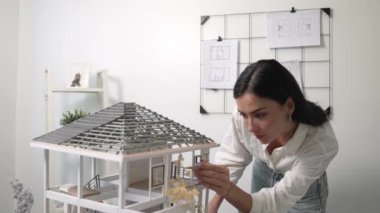 Genç, güzel ve zeki mühendisin yakın çekimleri modern ofiste duvarında taslak olan kalem kullanarak ev modelini ölçmeye odaklanıyor. Yaratıcı yaşam ve tasarım konsepti. Tertemiz..