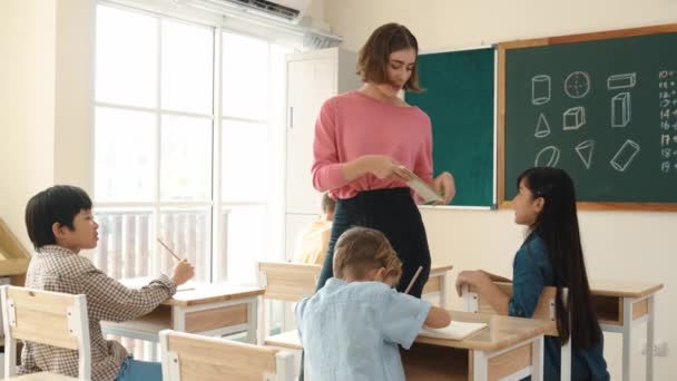 スマートアジアの学生が手を挙げ 教師が小学校の宿題を歩き チェックしながら数学の質問について先生に尋ねました 先生はノートを拾いながら質問に答える ペダゴロジー — ストック動画