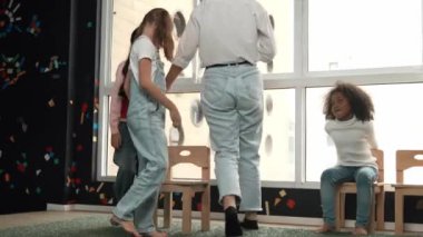 Çeşitli çocuklar sandalye kapmaca oynarken genç ve güzel öğretmenler müziği kapatıyor. Çok kültürlü öğrenciler yaratıcı aktivitelerde sandalyede koşup oturuyorlar. Müzik dersi. Etkinlik.