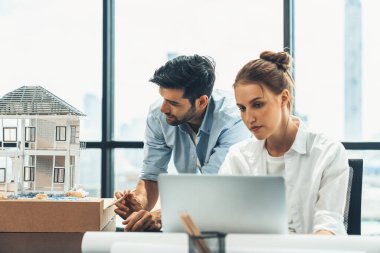 Genç yetenekli proje yöneticisi, modern ofis veya mimarlık stüdyosundaki proje planını kullanarak, Kafkas mühendisi ev modunu incelerken dizüstü bilgisayar kullanarak çalışıyor. İnşaat mühendisliği, yaratıcı tasarım. İzleme.