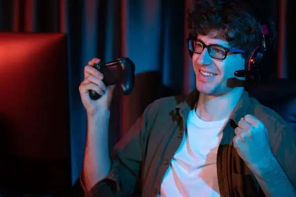 stock image Smiling young gaming streamer winning team playing with joystick on Esport online on pc fighting game to competitors on strategy planning for next harder at red neon lighting modern room. Gusher.